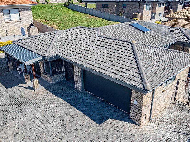 Aerial view of a brick house featuring a tiled roof with solar heating, a paved driveway, double garage, and a covered patio area.