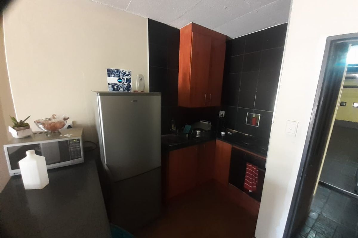 Compact kitchen featuring dark cabinetry, black tiled splashbacks, and integrated cooking appliances, offering a functional layout for an apartment setting.