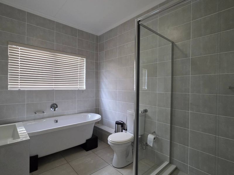 Modern bathroom featuring a freestanding bathtub, separate glass-enclosed shower, neutral ceramic tiling, and a clean, functional layout.