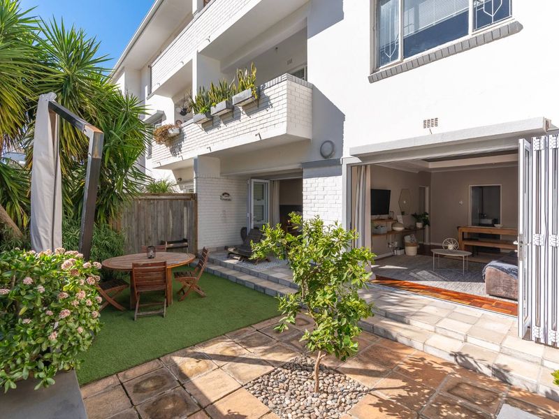 A well-maintained rear exterior view of an apartment featuring a paved patio, artificial lawn, and bi-fold doors leading into the living area.