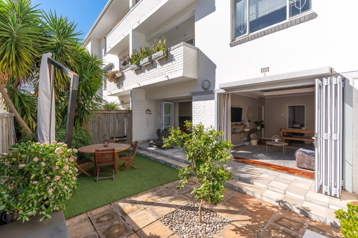A well-maintained rear exterior view of an apartment featuring a paved patio, artificial lawn, and bi-fold doors leading into the living area.