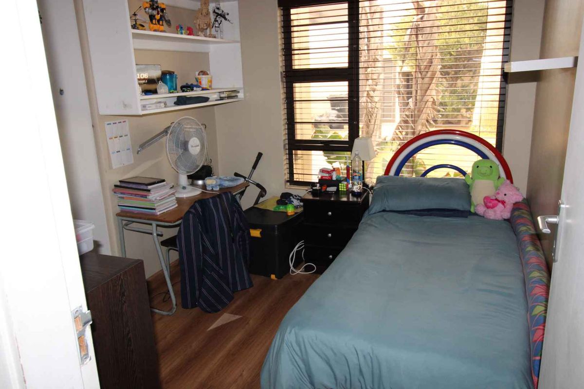 A functional bedroom featuring wood-look laminate flooring, a built-in wall shelf, and a large window with horizontal blinds.