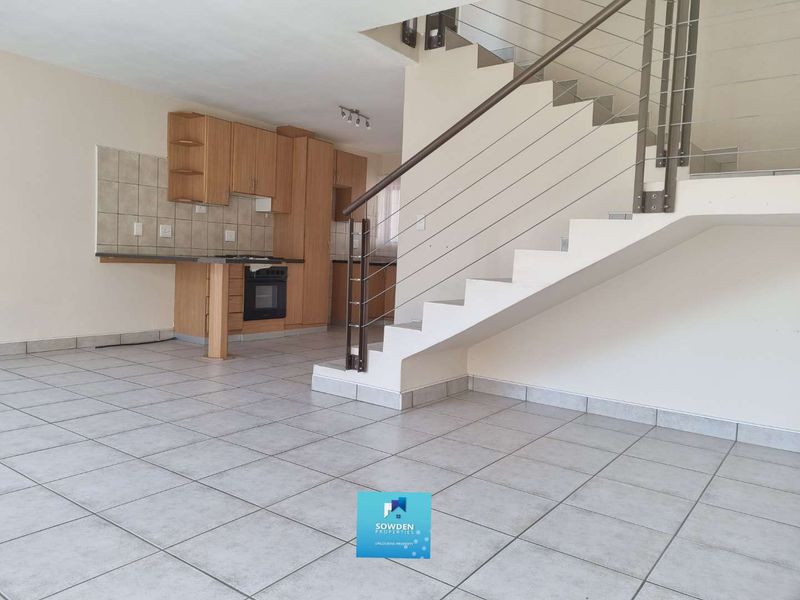 Open-plan living area featuring a functional kitchen with built-in cabinetry and oven, tiled flooring throughout, and a staircase with a modern metal balustrade.