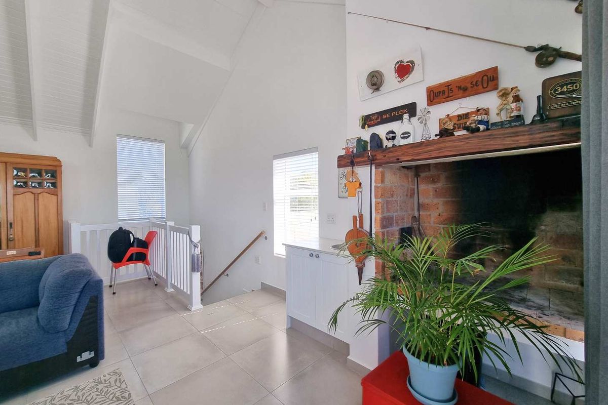 A bright living area featuring a vaulted ceiling, tiled flooring, and a prominent brick fireplace with a wooden mantelpiece.