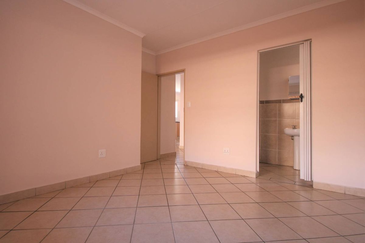 An empty living area featuring neutral tiled flooring and access to an adjoining bathroom with a pedestal basin.