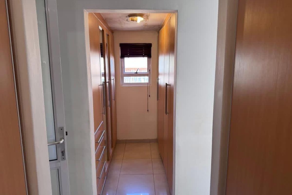 A narrow walk-in closet or dressing area featuring built-in wooden cabinetry, tiled flooring, and a small window for natural light.