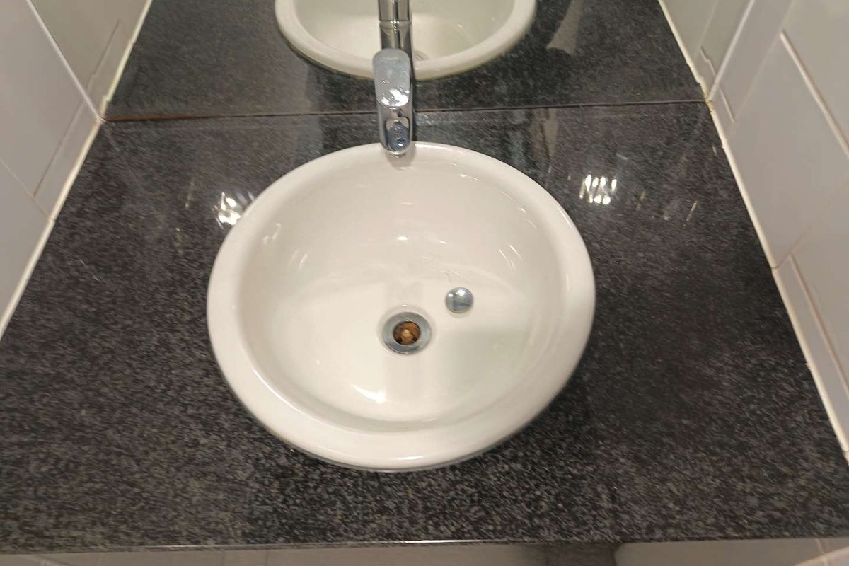 A close-up view of a bathroom vanity featuring a white drop-in basin set into a dark granite countertop with a chrome faucet.