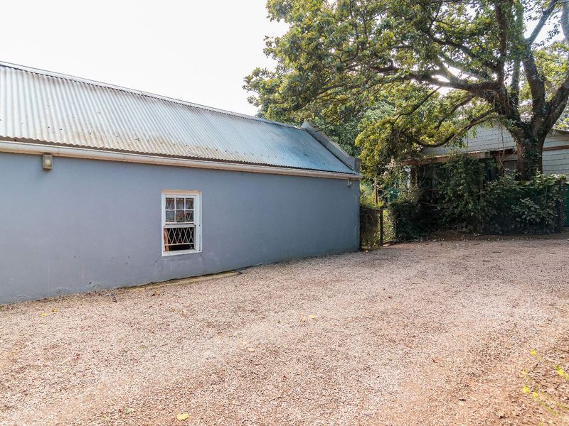 Rear exterior view of the property featuring a gravel driveway, corrugated metal roofing, and a single timber-framed window set into a painted masonry wall.