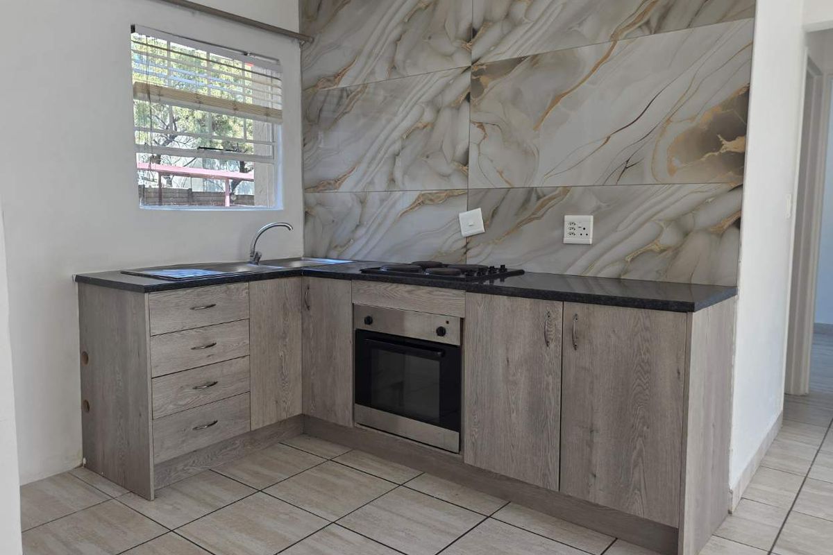 A modern kitchen featuring wood-grain cabinetry, dark stone countertops, a built-in oven with gas hob, and a striking marble-effect tiled splashback.
