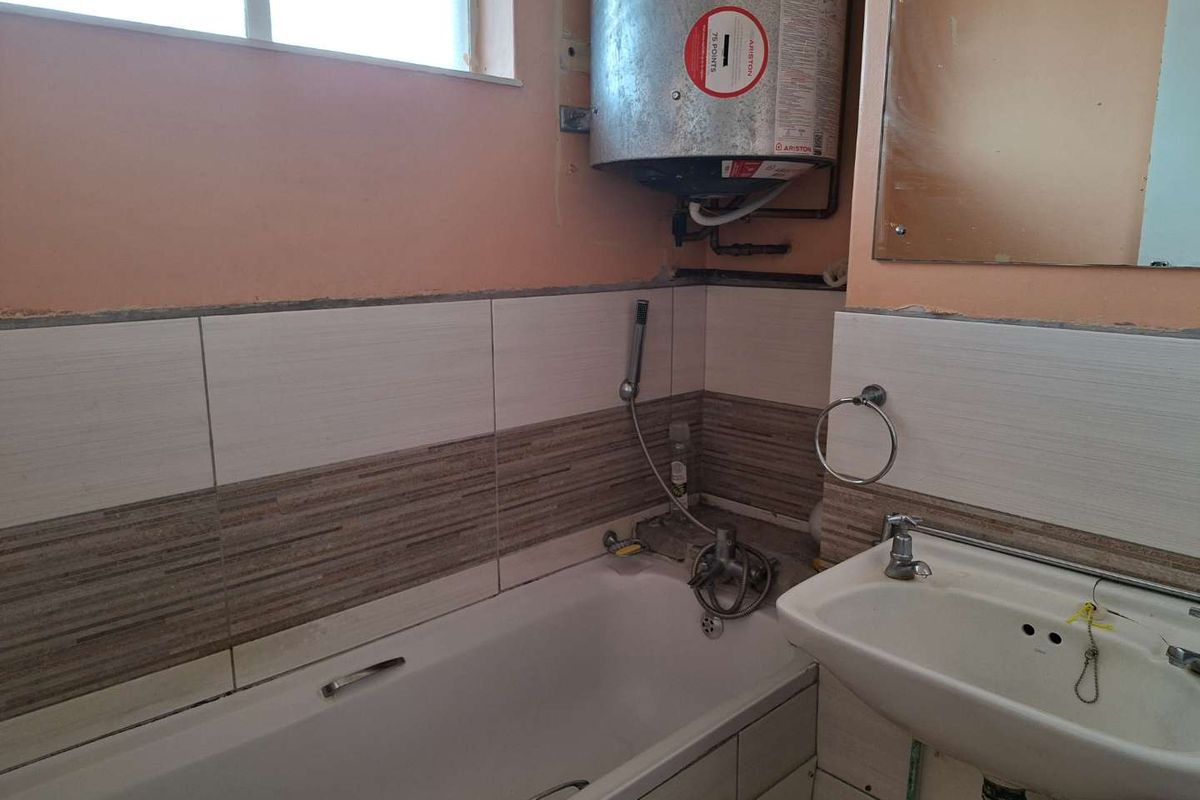 A dated bathroom featuring a bathtub, wall-mounted basin, and exposed electric water heater, requiring cosmetic updates and finish repairs.