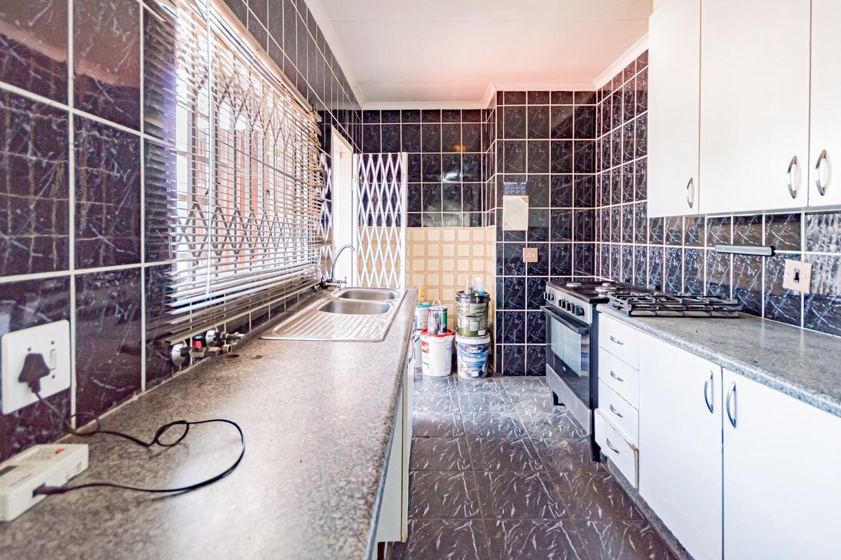 A dated kitchen featuring dark marble-effect wall tiles, white cabinetry, a stainless steel sink, and a freestanding gas stove.