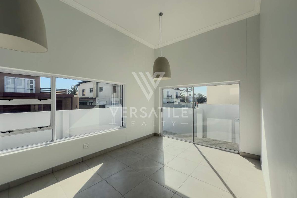 Bright and spacious living area featuring large windows, sliding glass doors, neutral tiled flooring, and modern pendant lighting.