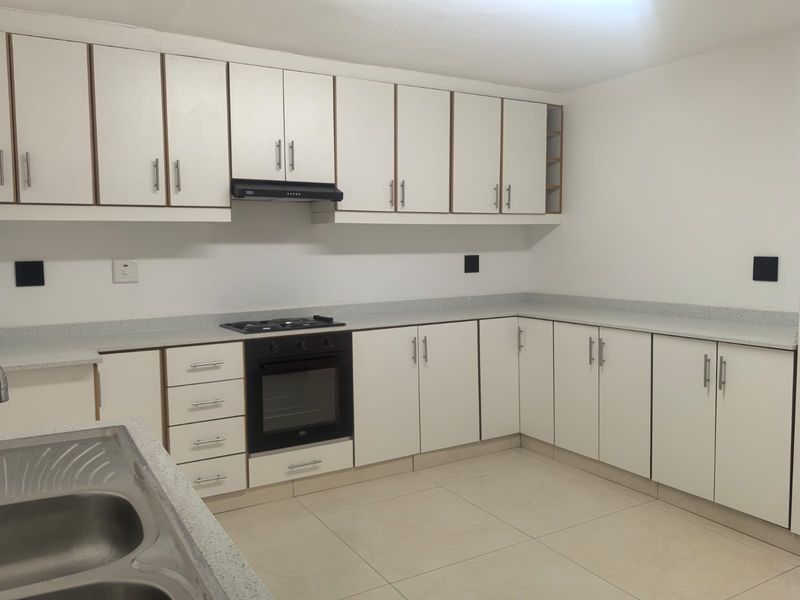 A clean, functional kitchen featuring white cabinetry, stone-look countertops, built-in oven, gas hob, and a double bowl stainless steel sink.
