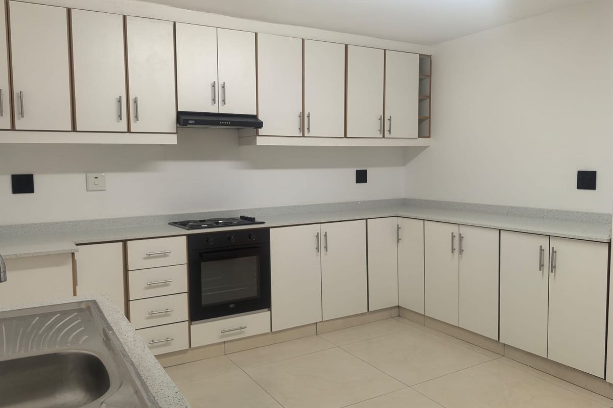 A clean, functional kitchen featuring white cabinetry, stone-look countertops, built-in oven, gas hob, and a double bowl stainless steel sink.