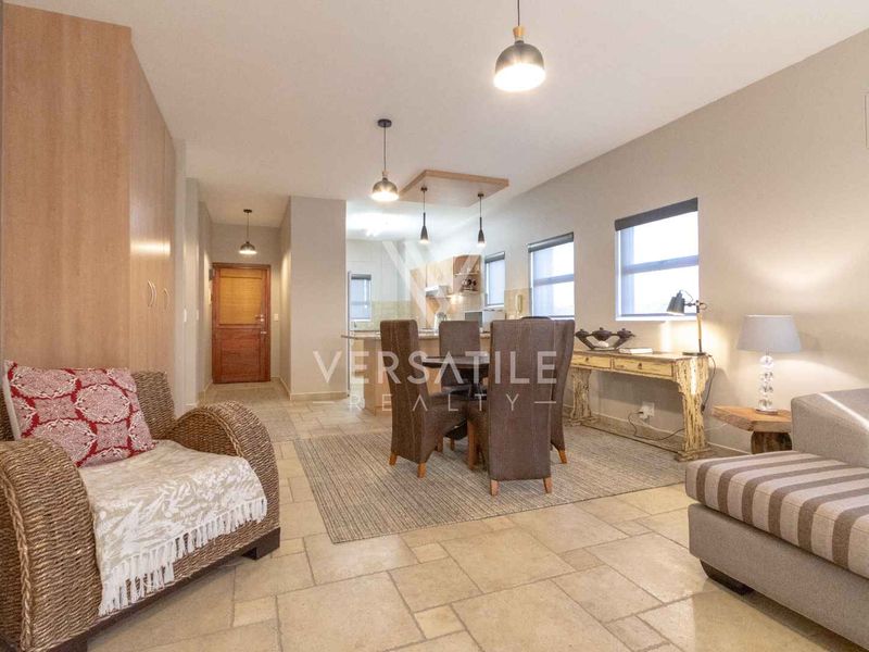 An open-plan living and dining area featuring tiled flooring, neutral walls, and integrated kitchen cabinetry with modern pendant lighting.