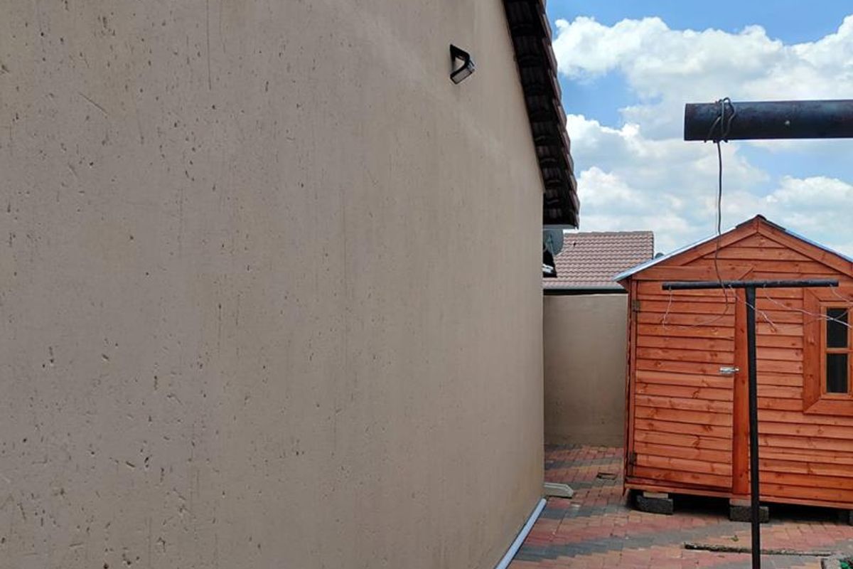 Side exterior view of the property featuring a paved walkway, satellite dish, and a wooden storage shed.