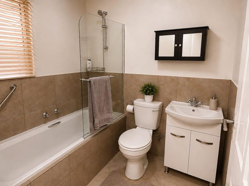 A functional bathroom featuring a bathtub with a glass screen, a vanity unit with a washbasin, and a wall-mounted medicine cabinet.