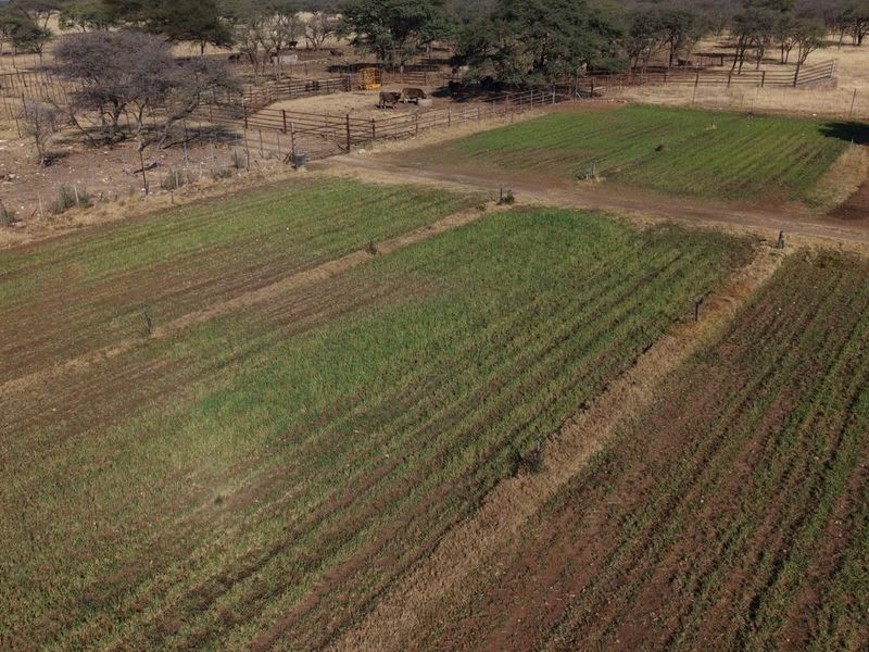 Aerial view of the farm property featuring cultivated agricultural land, livestock enclosures, and perimeter fencing.
