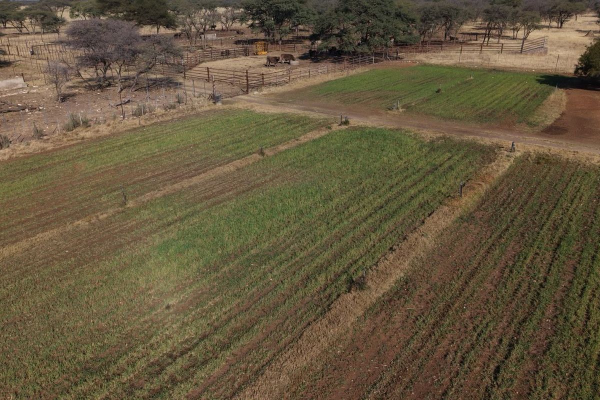 Aerial view of the farm property featuring cultivated agricultural land, livestock enclosures, and perimeter fencing.