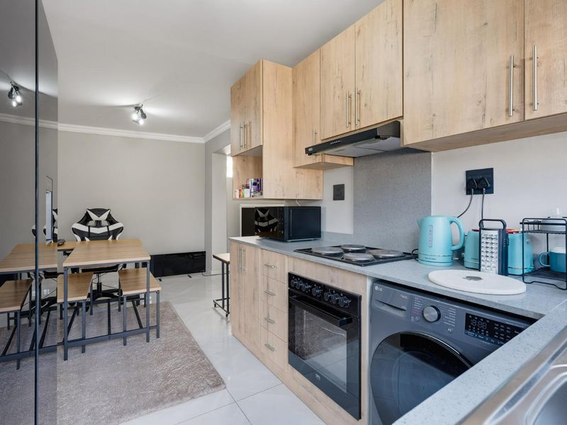 Modern open-plan kitchen and dining area featuring light wood-finish cabinetry, integrated appliances, and sleek tiled flooring.
