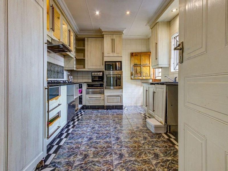 A dated kitchen featuring built-in cabinetry, integrated oven and microwave, gas hob, and tiled flooring. The space requires cosmetic updates to cabinetry and finishes.