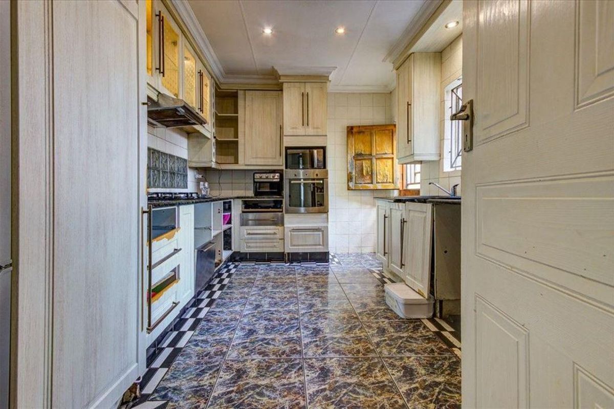 A dated kitchen featuring built-in cabinetry, integrated oven and microwave, gas hob, and tiled flooring. The space requires cosmetic updates to cabinetry and finishes.