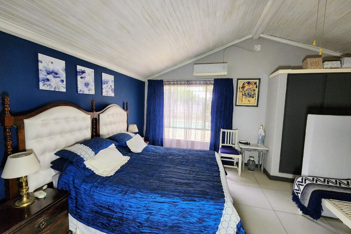 Spacious bedroom featuring a vaulted timber ceiling, tiled flooring, and a built-in wardrobe, complemented by a split-system air conditioner for climate control.