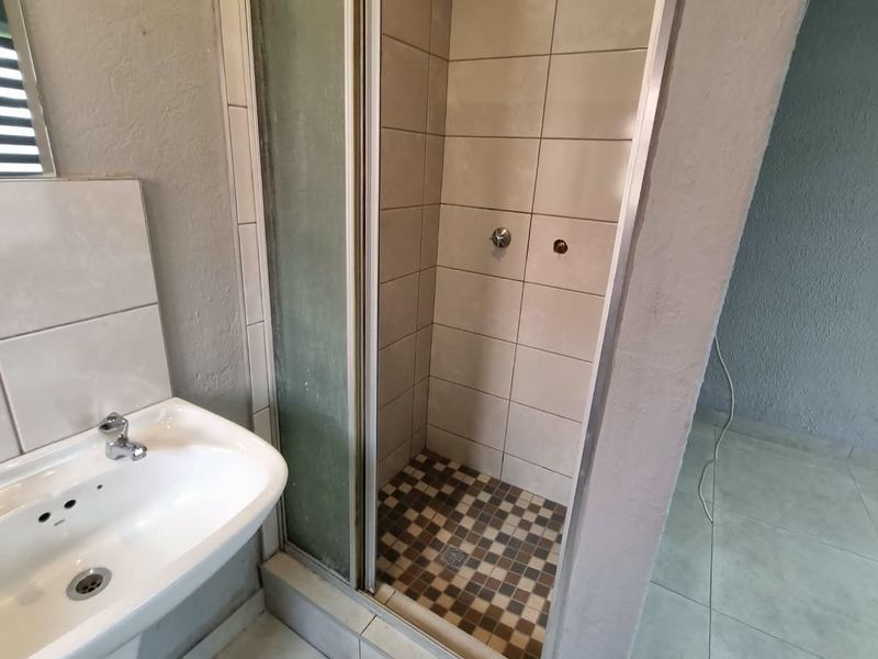 A functional bathroom featuring a pedestal basin and a tiled shower enclosure with a glass door.