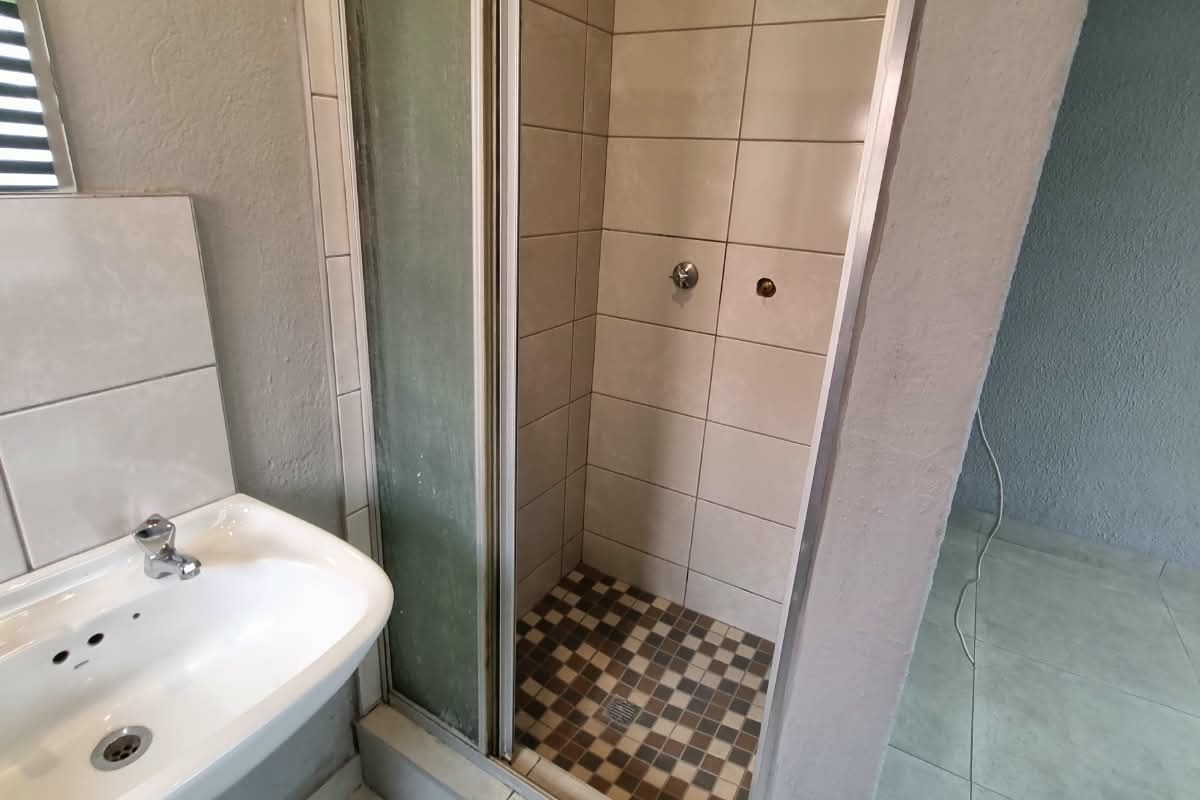 A functional bathroom featuring a pedestal basin and a tiled shower enclosure with a glass door.