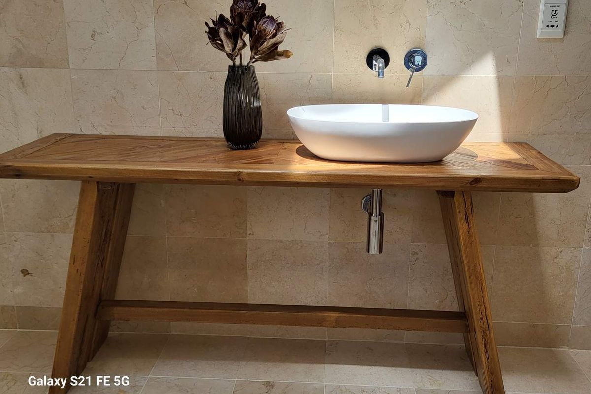A modern bathroom vanity area featuring a white vessel sink, wall-mounted chrome faucet, and elegant stone wall and floor tiling.