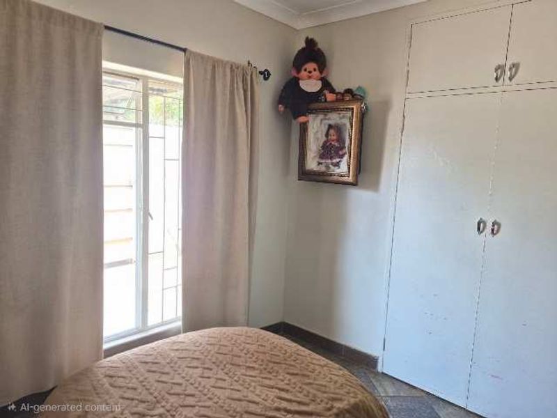 A functional bedroom featuring built-in cupboards, tiled flooring, and a window with security bars, offering a neutral space ready for personalization.