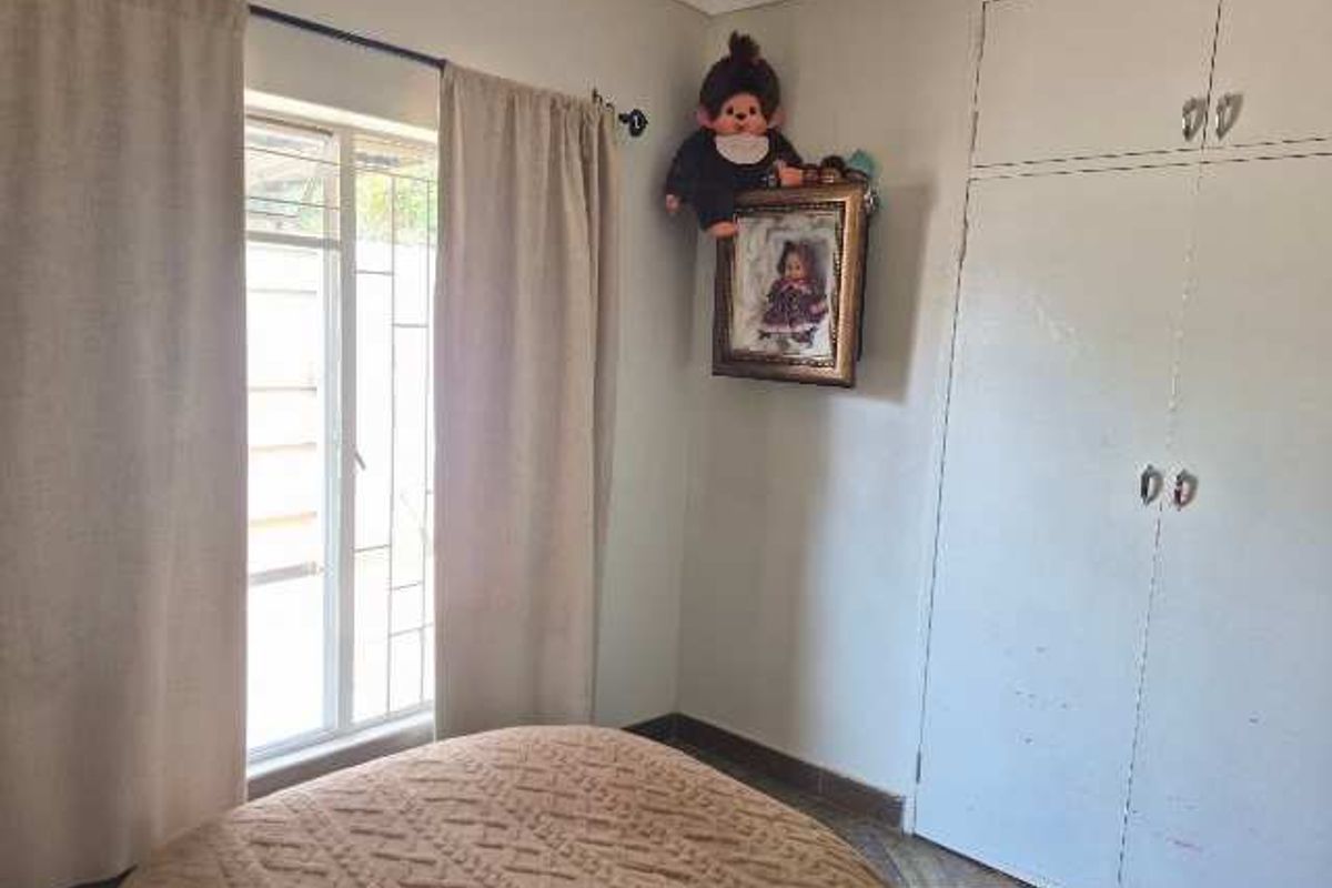A functional bedroom featuring built-in cupboards, tiled flooring, and a window with security bars, offering a neutral space ready for personalization.