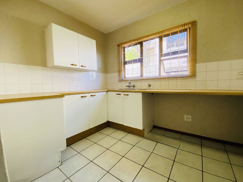 A functional kitchen featuring white cabinetry, laminate countertops, tiled backsplash, and ceramic flooring, offering a blank canvas for potential modern updates.