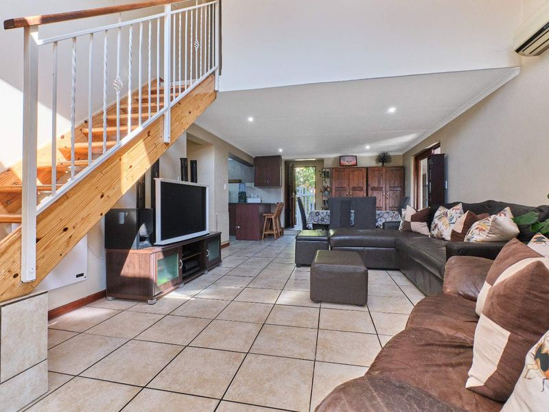 Spacious open-plan living area featuring ceramic floor tiles, a timber staircase with metal balustrade, and an integrated kitchen space.