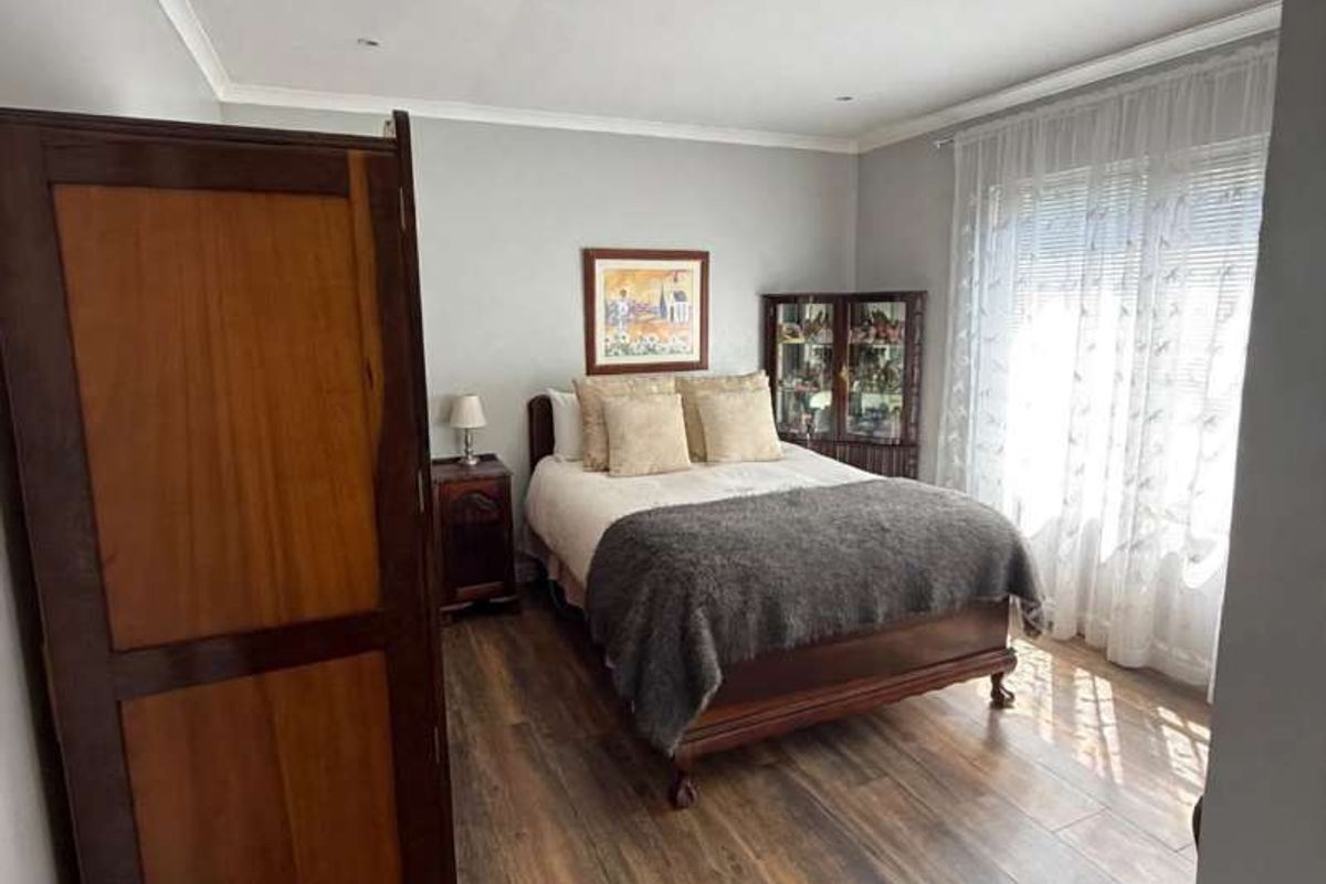 A well-maintained bedroom featuring modern laminate flooring, neutral wall tones, and recessed downlighting, offering a comfortable and inviting living space.