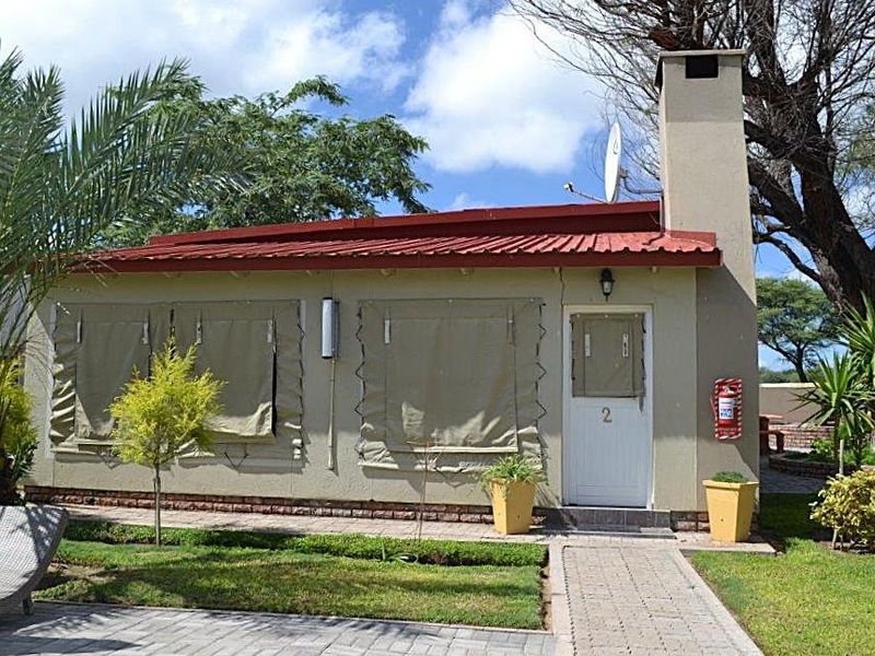 Exterior view of a guest house unit featuring a corrugated metal roof, brick chimney, and paved walkway access.