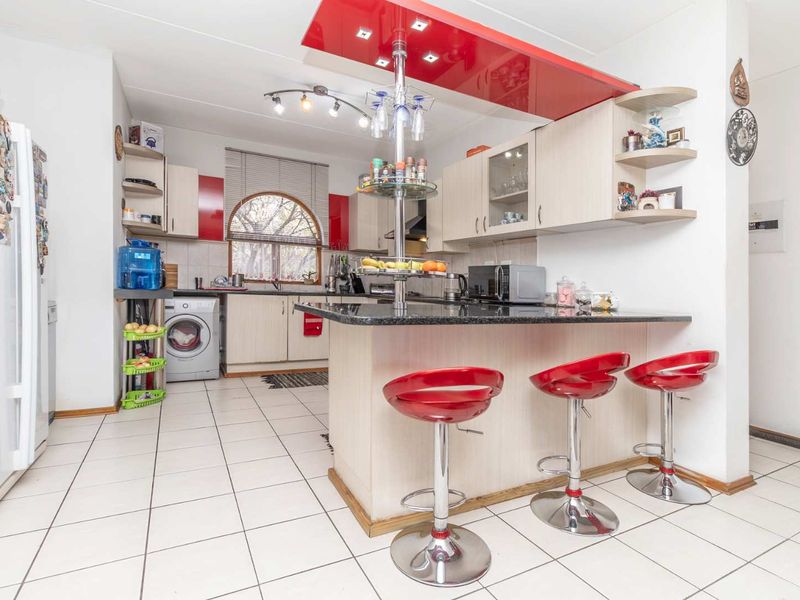A functional kitchen featuring granite countertops, a breakfast bar with overhead lighting, tiled flooring, and built-in cabinetry with a distinct red accent panel.