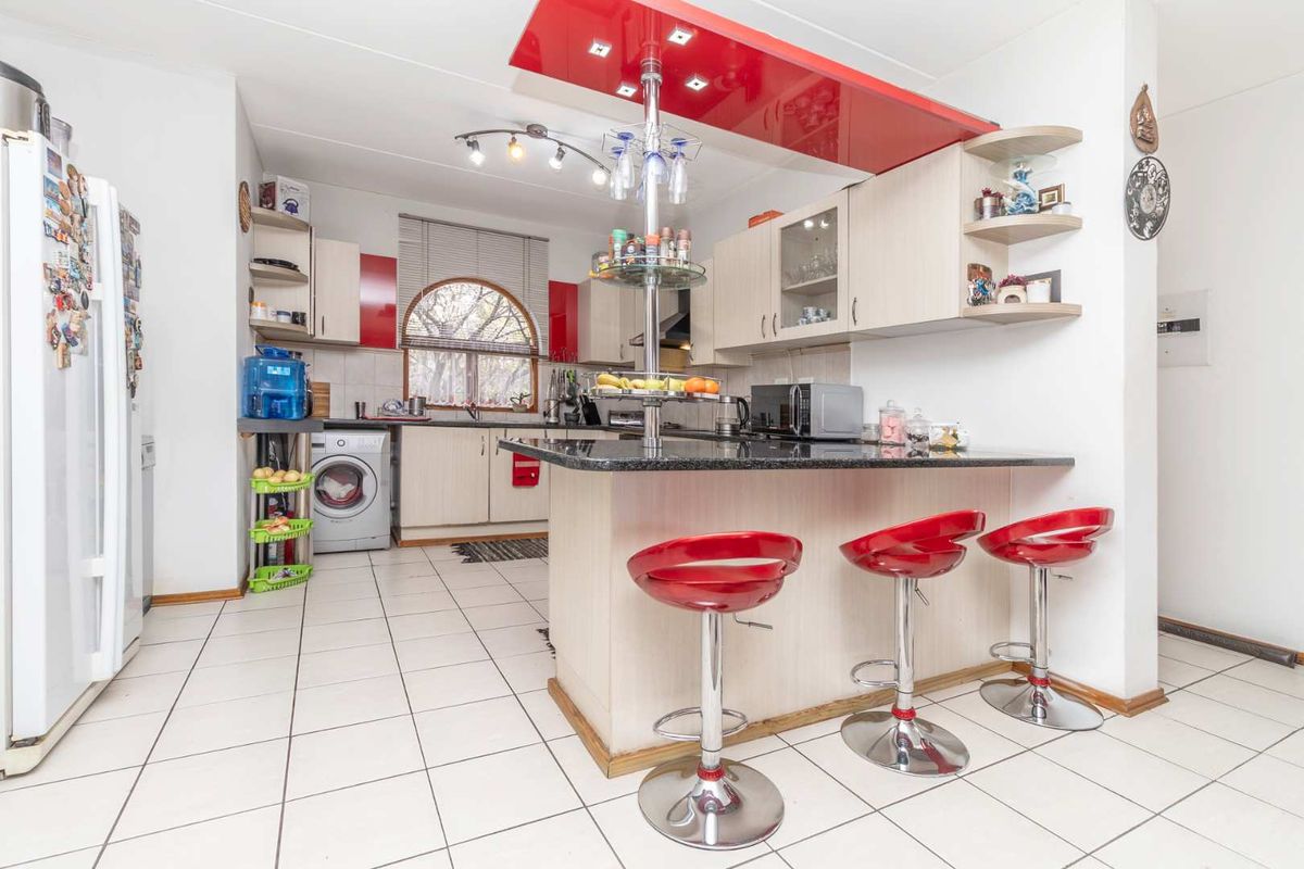 A functional kitchen featuring granite countertops, a breakfast bar with overhead lighting, tiled flooring, and built-in cabinetry with a distinct red accent panel.