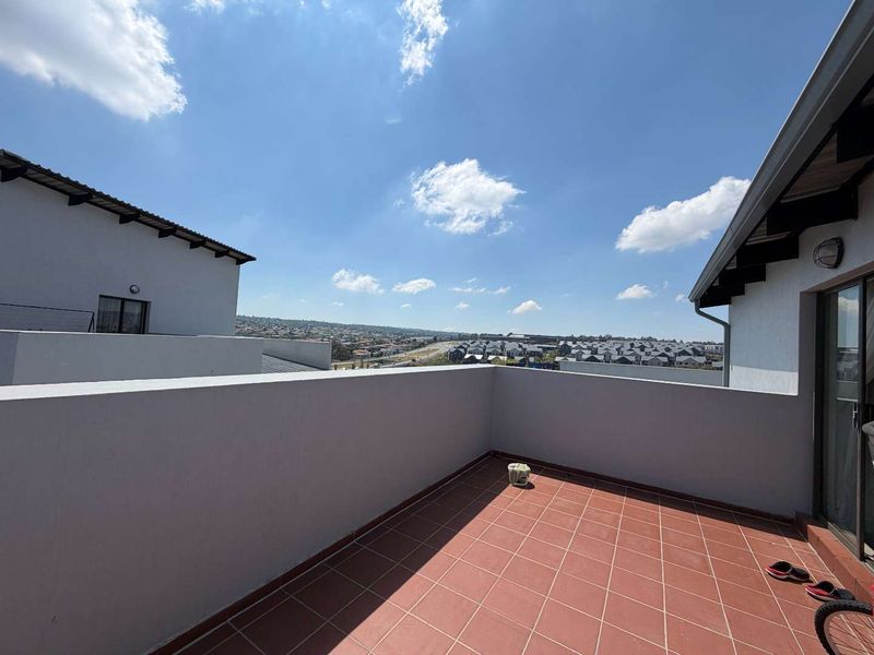 An open-air balcony featuring terracotta-style floor tiles and a solid parapet wall, offering expansive views of the surrounding residential area.