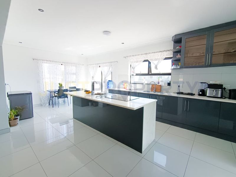 Modern open-plan kitchen featuring a large central island, sleek dark cabinetry, stone countertops, and polished ceramic tile flooring throughout the living space.