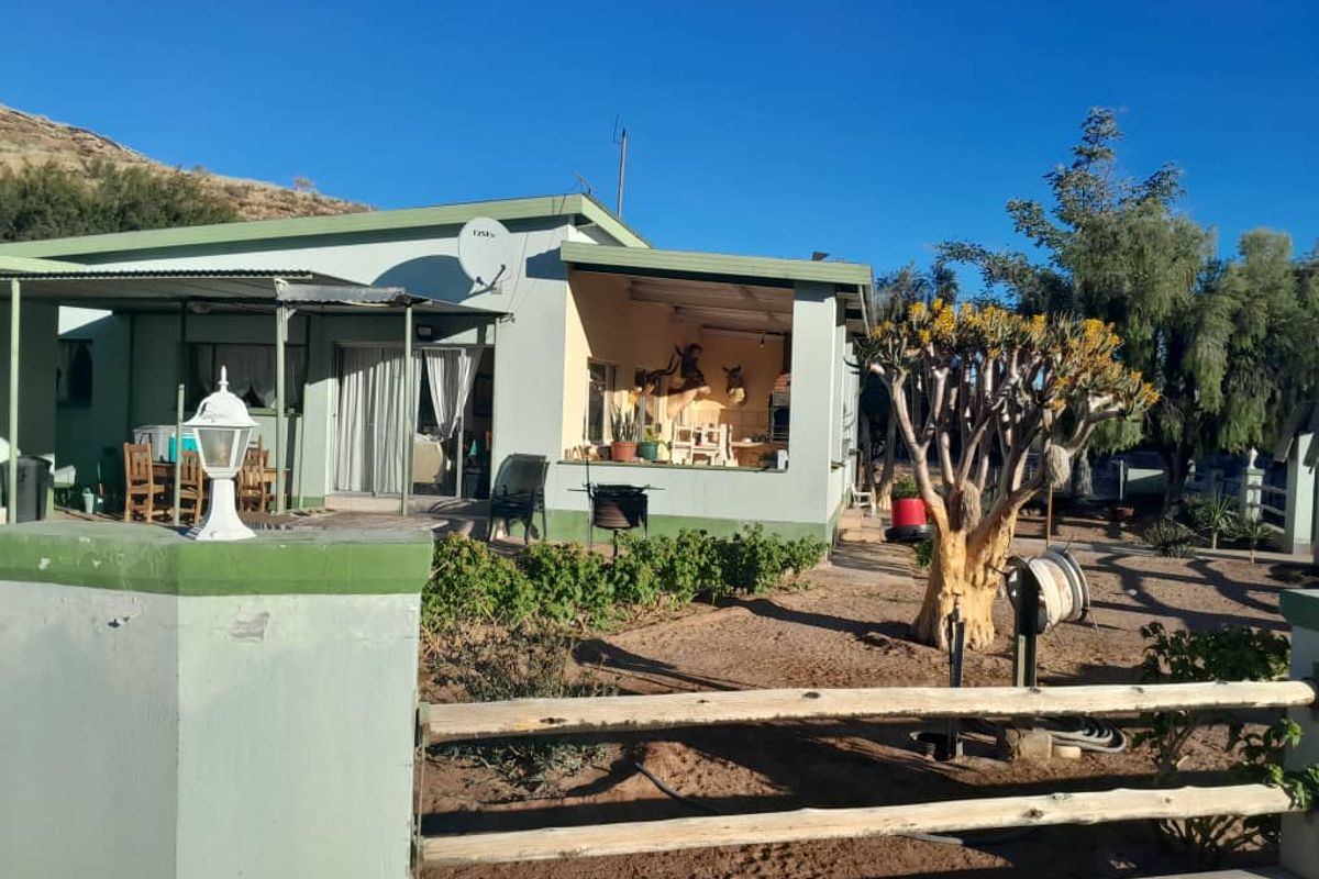 Rear view of the farmhouse featuring a covered patio area, sliding glass doors, and a surrounding garden with established trees and boundary fencing.