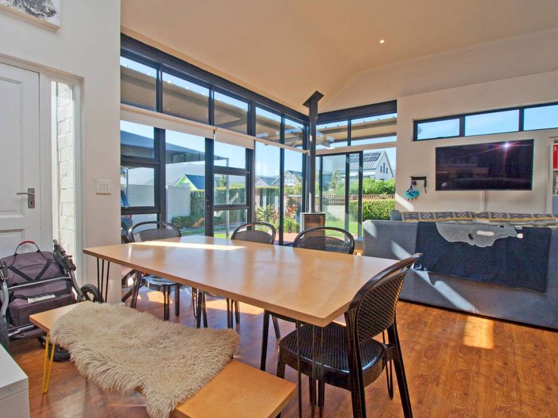 Bright open-plan living and dining area featuring vaulted ceilings, large black-framed windows, and a modern wood-burning fireplace.