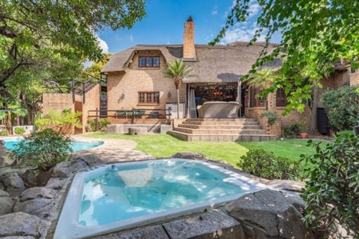Rear view of a charming thatched-roof cluster home featuring a landscaped garden, swimming pool, built-in jacuzzi, and a raised patio area.