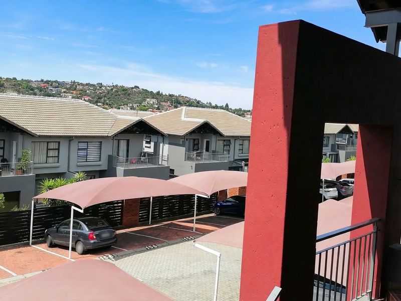 Elevated view overlooking a townhouse complex with paved parking areas, shade sail carports, and surrounding residential properties.