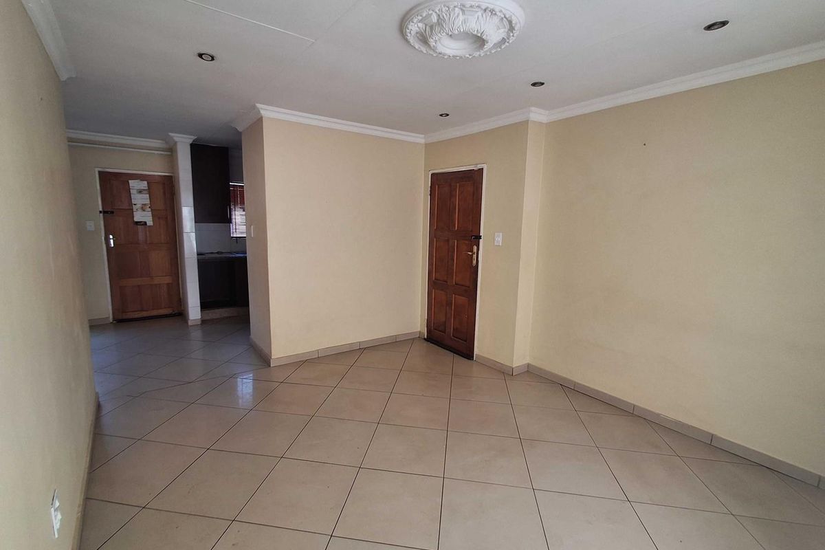 An empty living area featuring neutral tiled flooring, recessed downlighting, decorative ceiling rose, and classic timber panel doors leading to adjacent spaces.