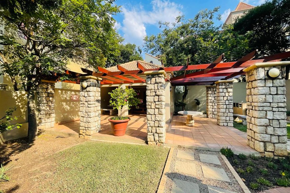 A spacious rear patio area featuring stone pillars, a timber pergola, and tiled flooring, overlooking a landscaped garden with a paved walkway.