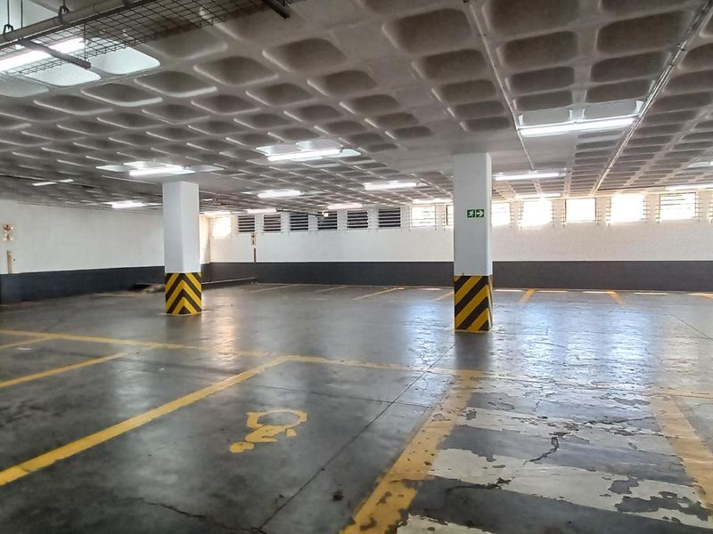 A spacious, open-plan underground parking garage featuring a waffle slab ceiling, fluorescent lighting, and marked parking bays.