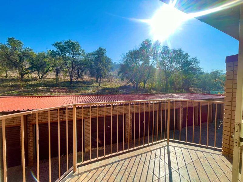 A balcony overlooking a row of brick garages with a metal balustrade and tiled flooring, offering an elevated view of the surrounding landscape.