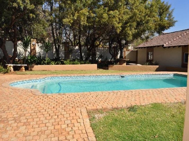 Outdoor pool area featuring a swimming pool, brick paved surround, and landscaped garden with retaining walls.