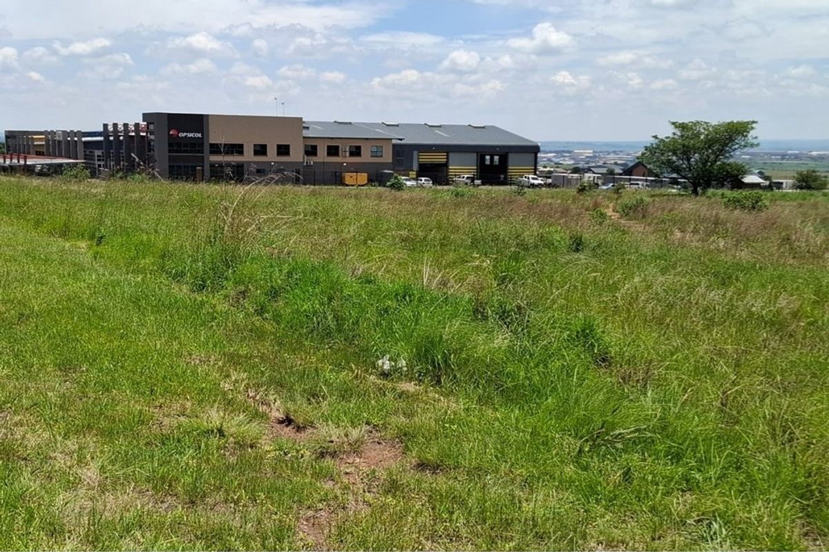 A view of a vacant residential plot featuring natural grass coverage with surrounding commercial and industrial infrastructure in the background.